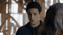 a young man with curly hair is standing next to a woman and talking to her .