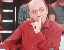 a man in a red shirt is holding his finger to his mouth