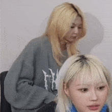 two blonde women are sitting next to each other in a room . one of the women is wearing a grey sweater .