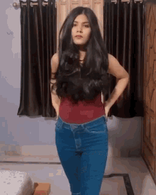 a woman with long black hair is standing in a room with her hands on her hips .