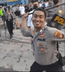 a police officer is smiling while holding a baton in front of a crowd of people .