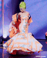 a woman with green hair is dancing on a stage in a floral dress .