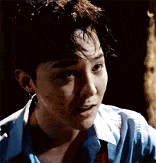 a close up of a man 's face with blood on it . he is wearing a blue shirt and earrings .