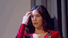a woman in a red floral dress is touching her hair and looking at the camera .