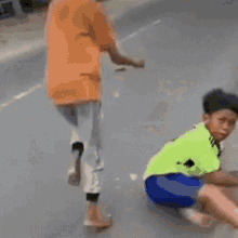 a young boy wearing a green shirt and blue shorts is squatting down on the ground .