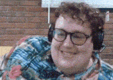a man wearing headphones and glasses is smiling and sitting on a couch .