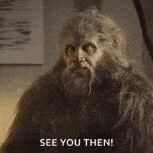a man dressed as a bigfoot with a beard is sitting in a room and says `` see you then '' .