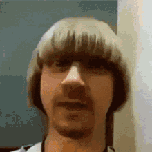 a man with blonde hair and a mustache is looking at the camera .