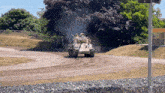 a military tank is driving down a dirt road with smoke coming out of it