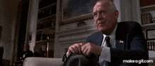 a man in a suit and tie sits at a desk in a room .