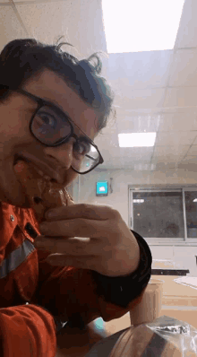 a man wearing glasses is eating a sandwich in a room