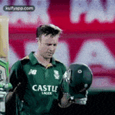 a man in a green shirt is holding a helmet in his hand .