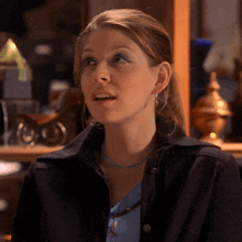 a woman wearing a blue necklace and a black jacket looks to the side
