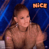 a woman wearing a gold top and earrings is clapping her hands in front of a blue background .