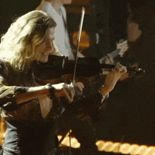 a woman playing a violin with a man behind her