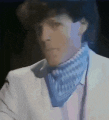 a man in a white suit and a blue scarf around his neck