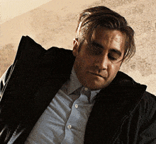 a man wearing a black jacket and a blue shirt looks down