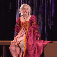 a woman in a red and pink dress with a yellow trim is sitting down