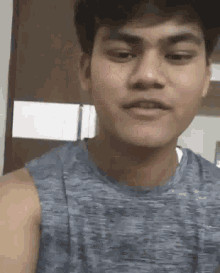 a young man is wearing a gray tank top and making a funny face .