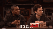 two men sitting at a table with a box that says it 's cool on it