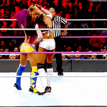 two women are wrestling in a wrestling ring while a referee looks on .