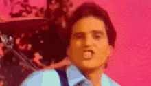 a man in a blue shirt and tie is making a funny face against a pink background