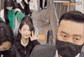 a man wearing a mask is standing in front of a crowd of people and waving at the camera .