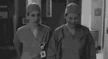 a black and white photo of a nurse standing next to a patient in a hospital .