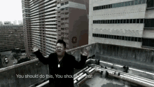 a man stands on a rooftop with his arms outstretched and says " you should do this you should do what "