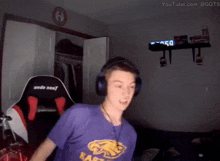 a man wearing headphones and a purple shirt is standing in a dark room .