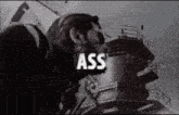 a man with a beard and sunglasses is standing in front of a building with the word ass on it .