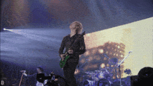 a man playing a guitar in front of a drum set with the letter d on the bottom
