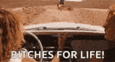 two women are driving a car with the words `` bitches for life '' written on the dashboard .