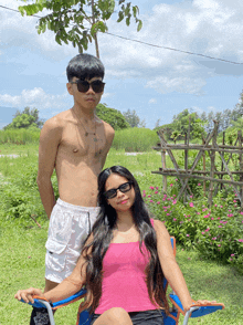 a man without a shirt stands next to a woman wearing sunglasses and a pink tank top