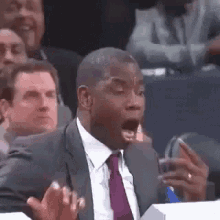 a man in a suit and tie is sitting in a stadium with his mouth open and a surprised look on his face .