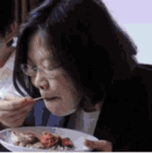 a woman with glasses is eating a plate of food with a spoon .