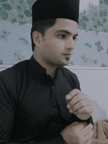 a man wearing a black shirt and a black hat is sitting in front of a wall with butterflies on it