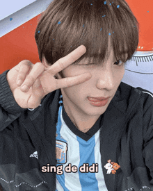a boy wearing a shirt that says sing de didi shows a peace sign