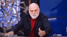 a man with a beard is giving a thumbs up in front of a nbc sign