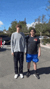 two young men are standing next to each other in a parking lot . one of the men is wearing a striped sweater