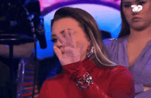 a woman in a red turtleneck covering her face with her hands