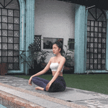 a woman sits on a yoga mat in front of a building with a window that says ' x ' on it