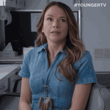 a woman in a denim dress sits in a chair with a box of tissues in the background