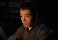 a young man in a traditional costume is sitting in a dark room looking at the camera .