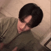 a young man with short black hair is wearing a green t-shirt