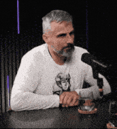 a man with a beard is sitting in front of a microphone wearing a white shirt with a soldier on it