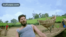 a man with a beard is standing in front of a wooden boat in a field .