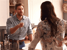 a man in a denim shirt is talking to a woman in a floral shirt in a kitchen