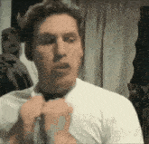 a man in a white shirt is adjusting his tie in a room .