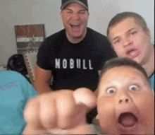 a man wearing a nobull shirt is pointing at the camera .